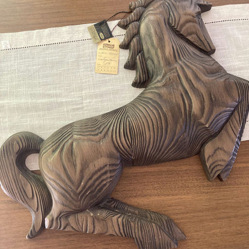 A wooden horse sculpture rests on a table, showcasing intricate grain patterns. A price tag is attached, indicating it is a decorative item.