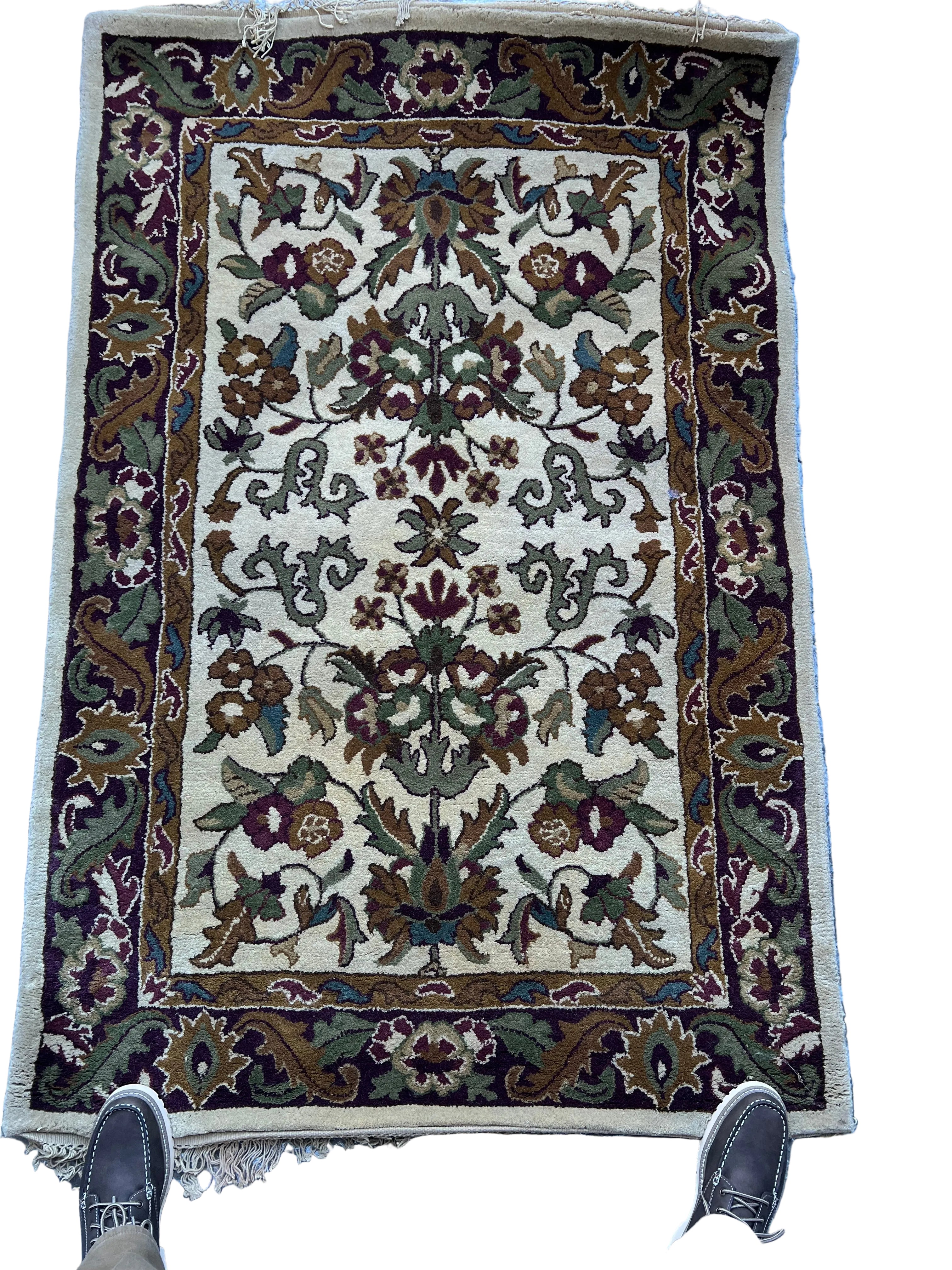 A floral-patterned rug featuring intricate designs in shades of cream, burgundy, green, and blue, laid out on a reflective surface.