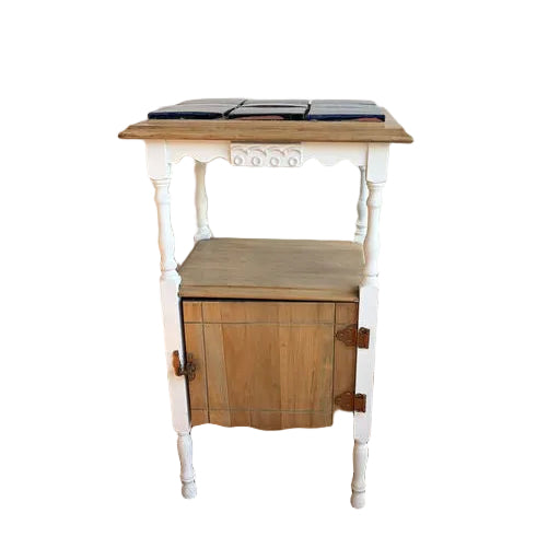 A small vintage side table with a white base and natural wood top, featuring a lower cabinet with a wood door and decorative legs.