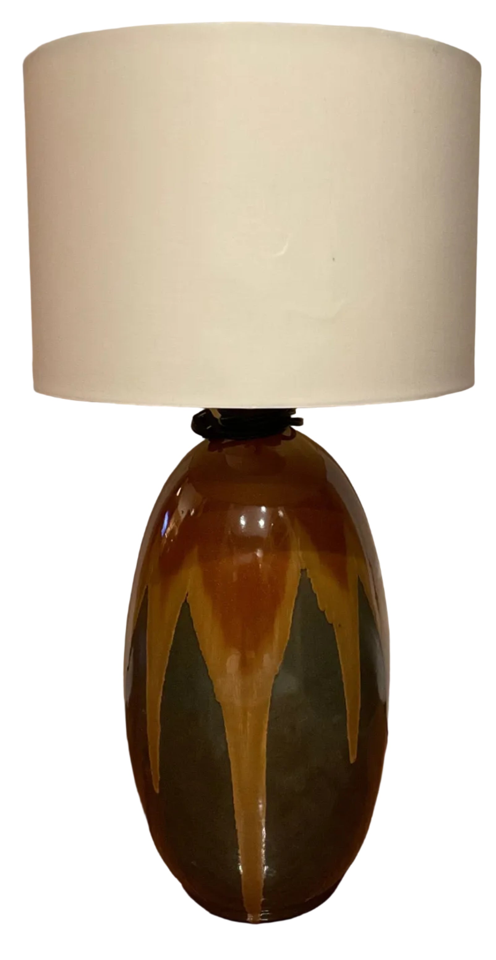 A decorative lamp with a ceramic base featuring earthy colors—brown, green, and orange—topped with a plain white fabric shade, positioned near a door.