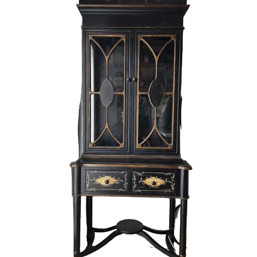 A vintage black cabinet with glass doors and decorative details stands in a well-lit room, featuring a lower drawer with floral designs.