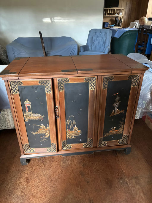 A wooden cabinet with intricate painted panels depicting scenes of boats and landscapes. It features a warm finish and ornate detailing.