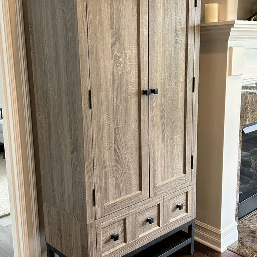 A wooden cabinet with a light oak finish and black hardware, featuring two doors and three drawers, stands against a wall in a cozy interior.
