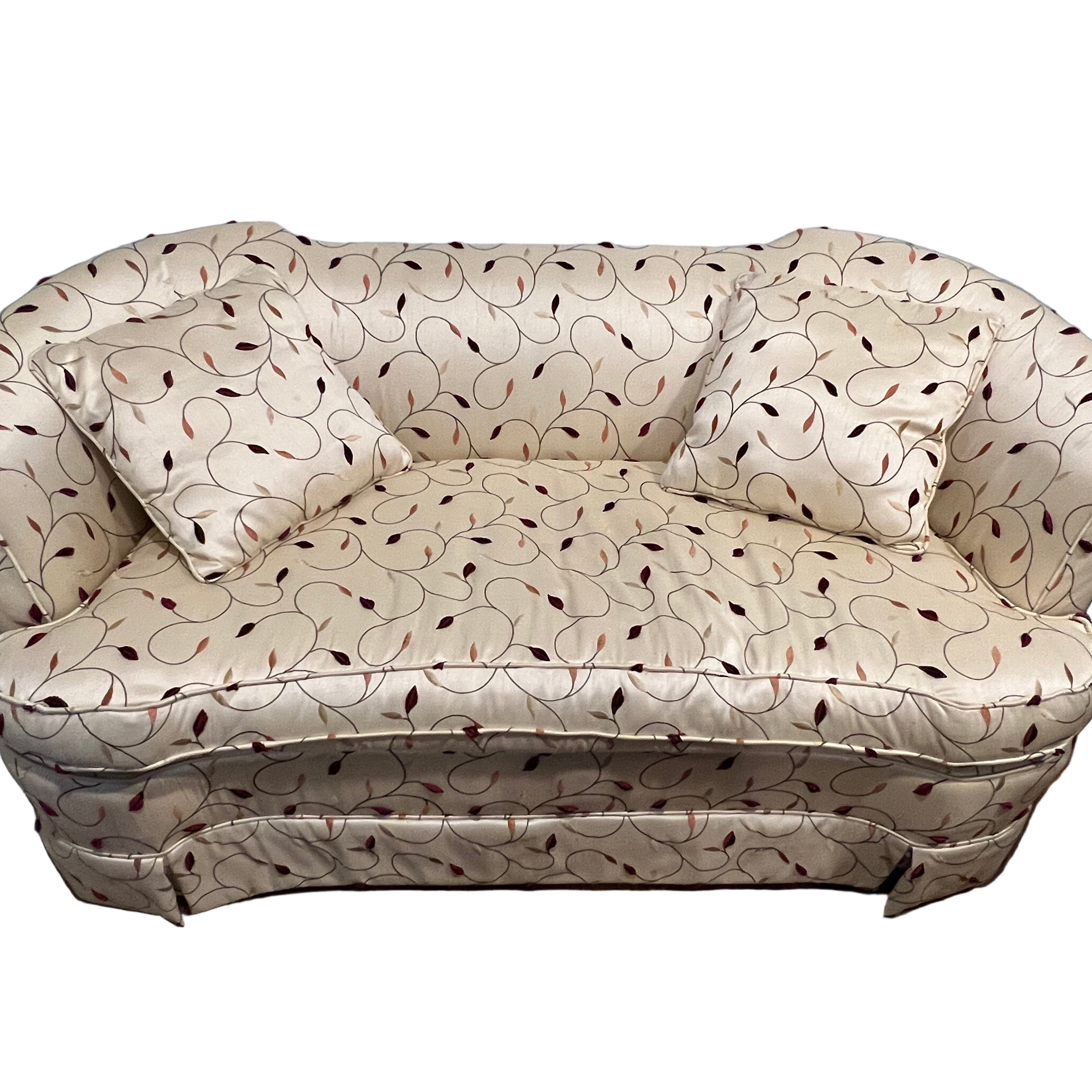 A plush, two-seater sofa with cream fabric featuring a subtle pattern of maroon leaves, accompanied by two matching, square cushions.