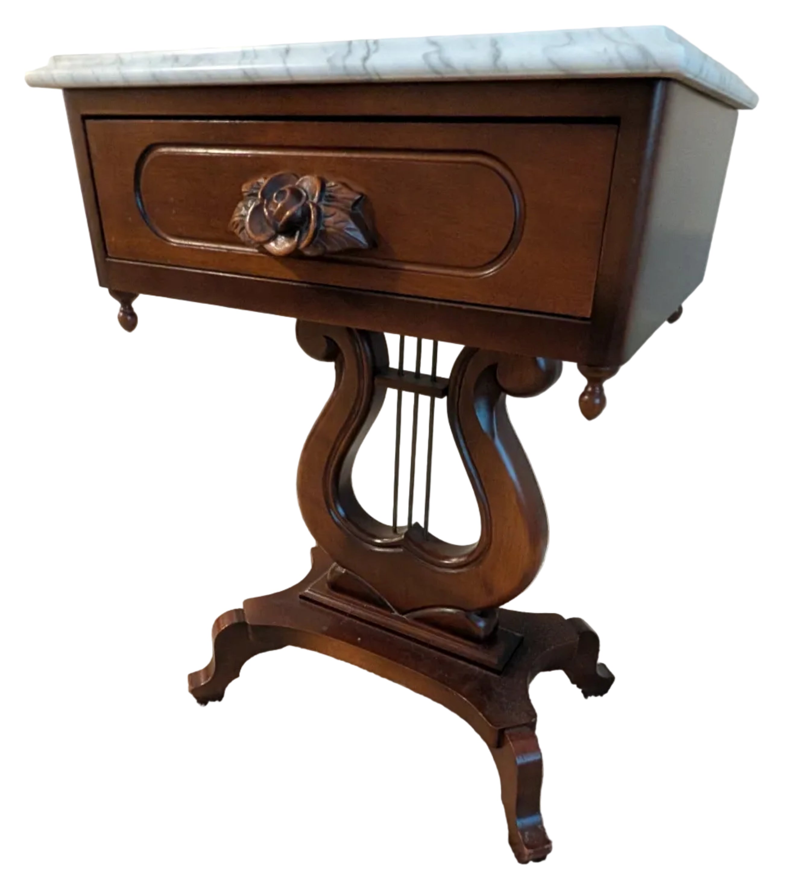 A wooden side table with a decorative marble top, featuring an ornate rose drawer handle and elegant curved legs, set on plush carpet.