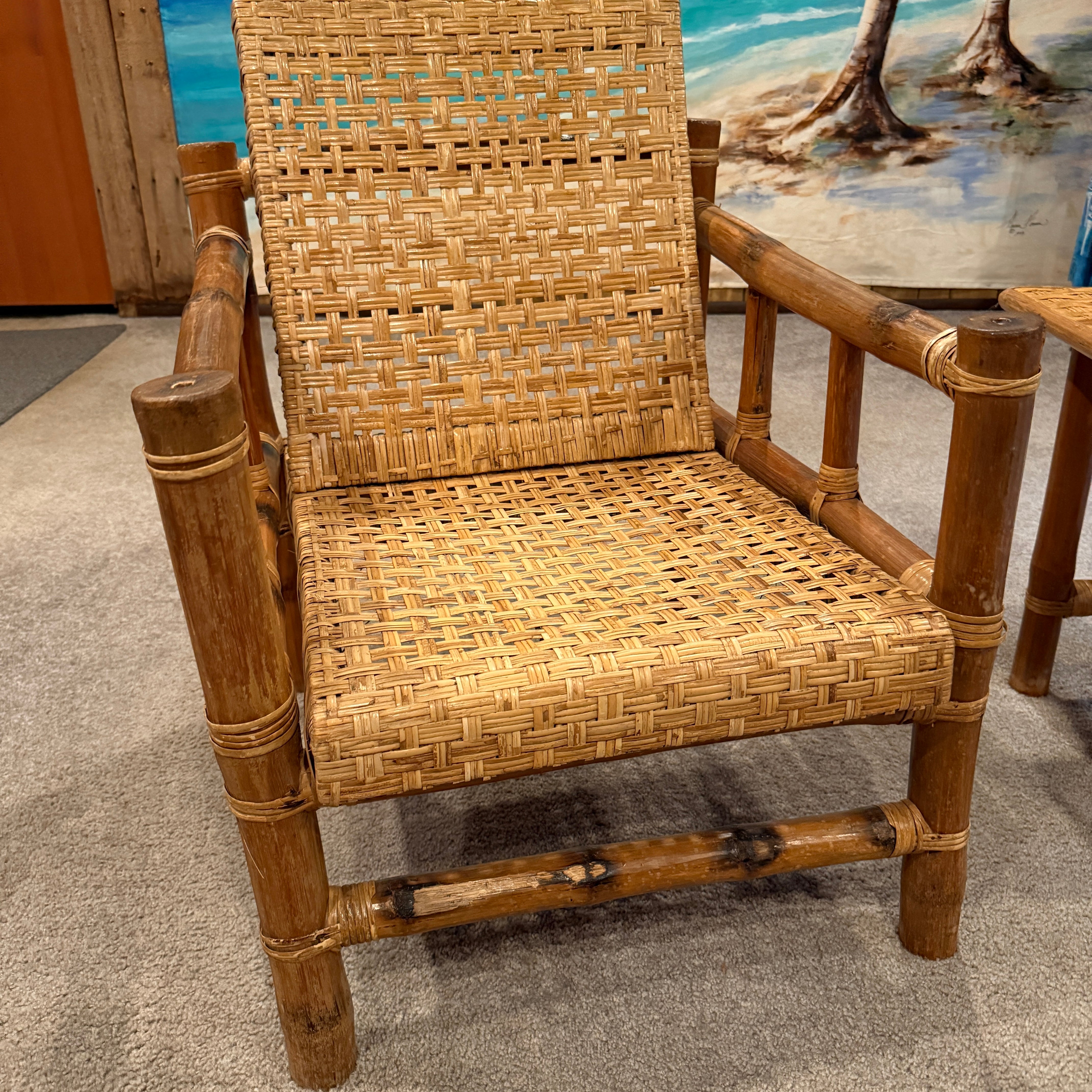 A woven bamboo chair with a natural finish sits on a carpeted floor, set against a colorful beach mural featuring ocean waves and palm trees.