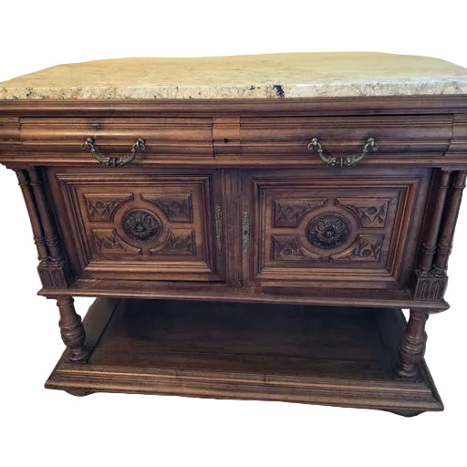 A wooden sideboard with ornate carvings and a marble top, featuring two cabinets with decorative doors and elaborate hardware, stands on a tiled floor.
