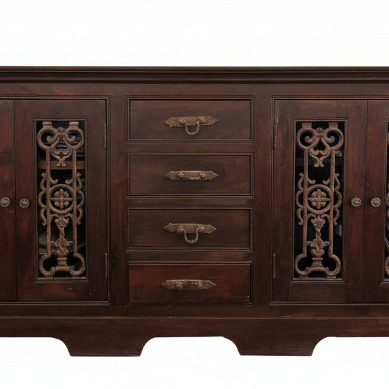 A wooden sideboard with intricate carvings, topped with a colorful table runner. Two framed artworks hang above it: one abstract, one floral.
