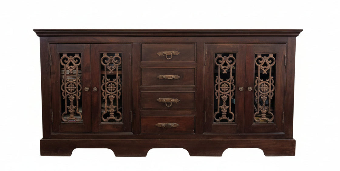 A wooden sideboard with intricate carvings, topped with a colorful table runner. Two framed artworks hang above it: one abstract, one floral.