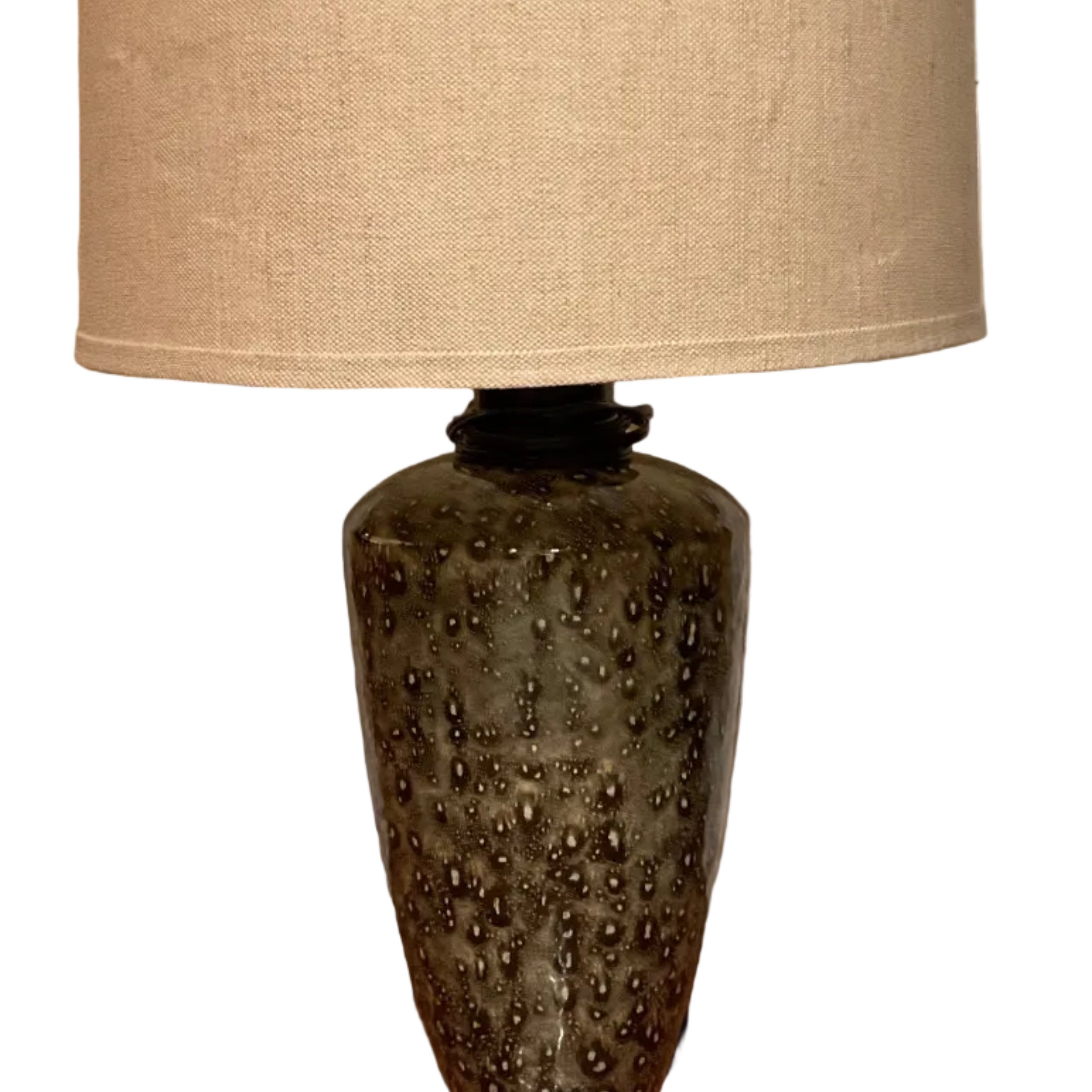 A decorative lamp with a patterned ceramic base and a beige fabric shade stands on wooden flooring next to a white door.