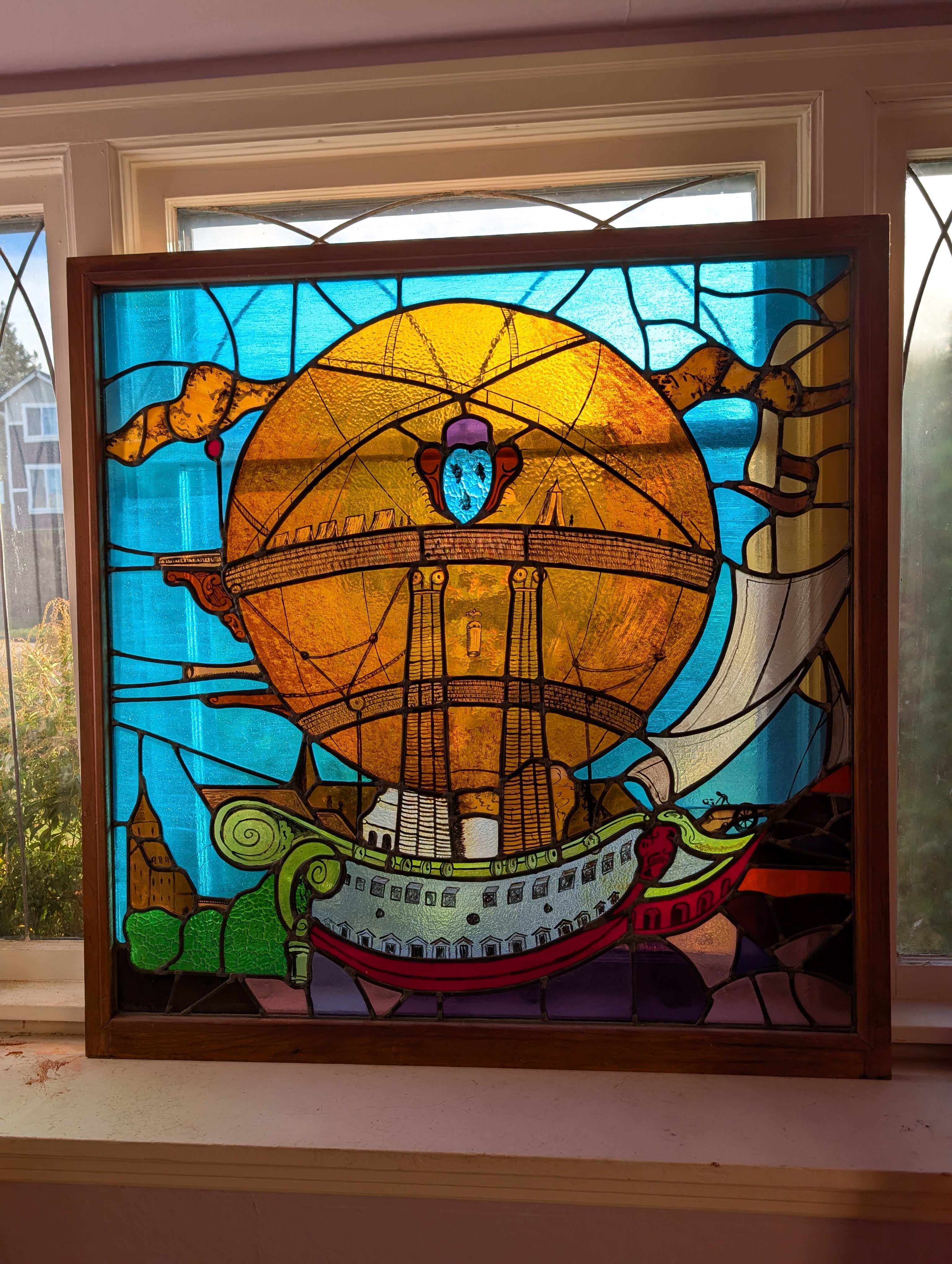 Vibrant stained glass artwork depicting a whimsical hot air balloon and ship against a blue sky, framed in wood, showcasing intricate detailing.