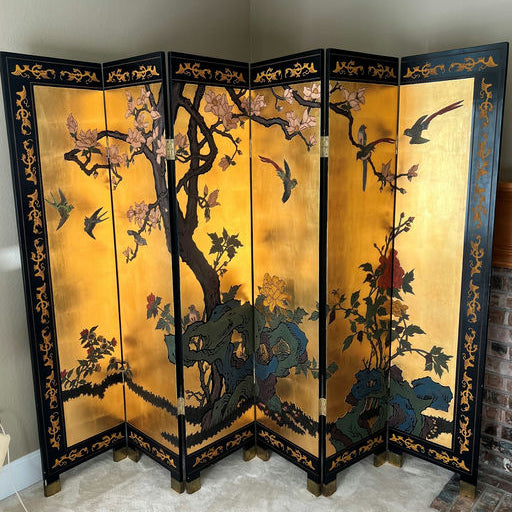 A decorative folding screen featuring intricate artwork of birds and flowers on a golden background, with black and gold accents.