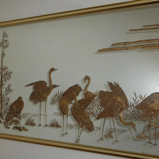 A decorative wall art piece featuring golden cranes among bamboo and water vegetation, framed elegantly, capturing a tranquil nature scene.