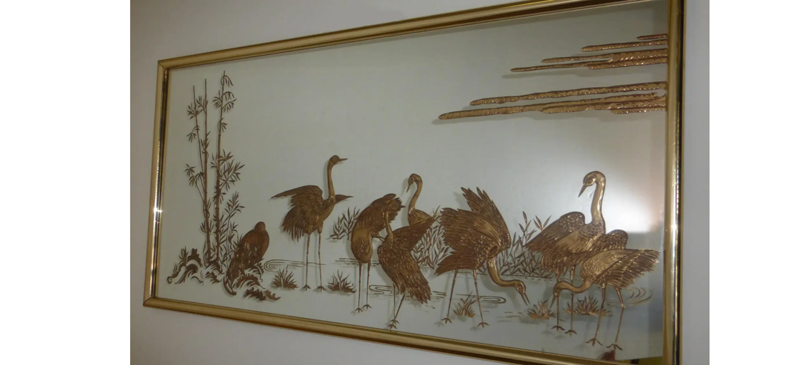 A decorative wall art piece featuring golden cranes among bamboo and water vegetation, framed elegantly, capturing a tranquil nature scene.