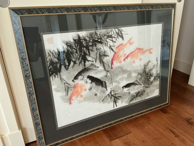 A framed artwork depicting colorful koi fish swimming amidst bamboo and watercolor splashes, displayed on a wooden floor.