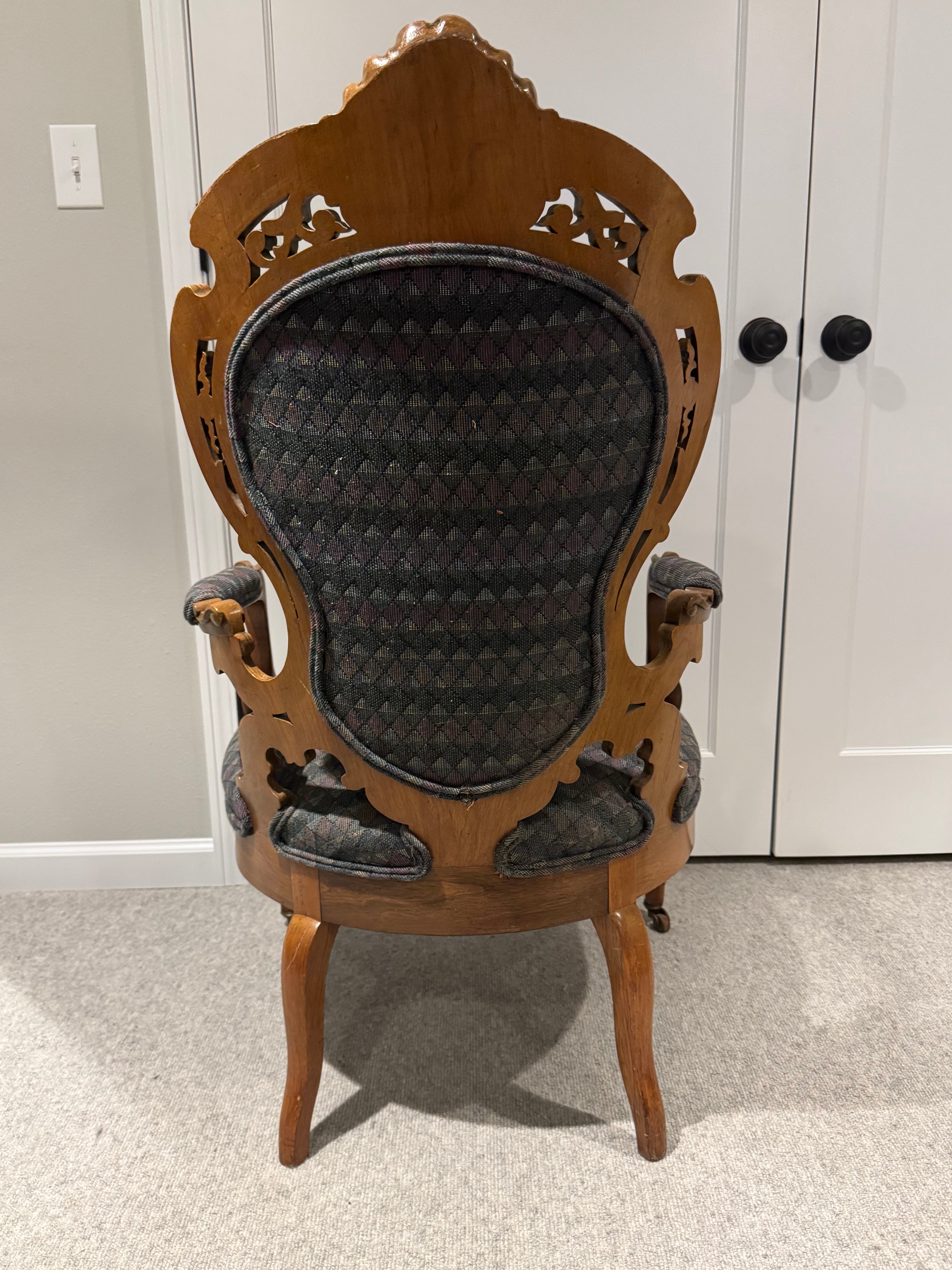 A vintage wooden chair with an ornate backrest and patterned upholstery sits on a light carpet, facing a pair of closed white doors.