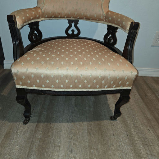 A vintage chair with a curved backrest and black wooden frame, upholstered in light orange fabric featuring a subtle pattern, placed on a wood floor.