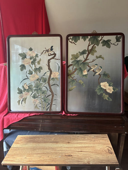 Two decorative panels featuring stylized floral designs and perched birds, set against a neutral background, displayed on a wooden table.