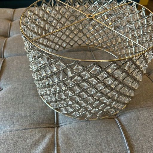 A decorative crystal basket with a diamond pattern sits on a gray tufted surface, reflecting light beautifully in a cozy living space.