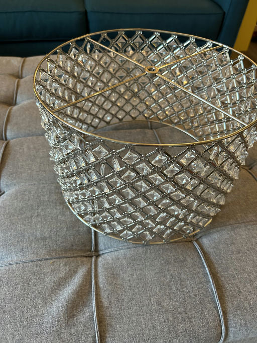 A decorative crystal basket with a diamond pattern sits on a gray tufted surface, reflecting light beautifully in a cozy living space.