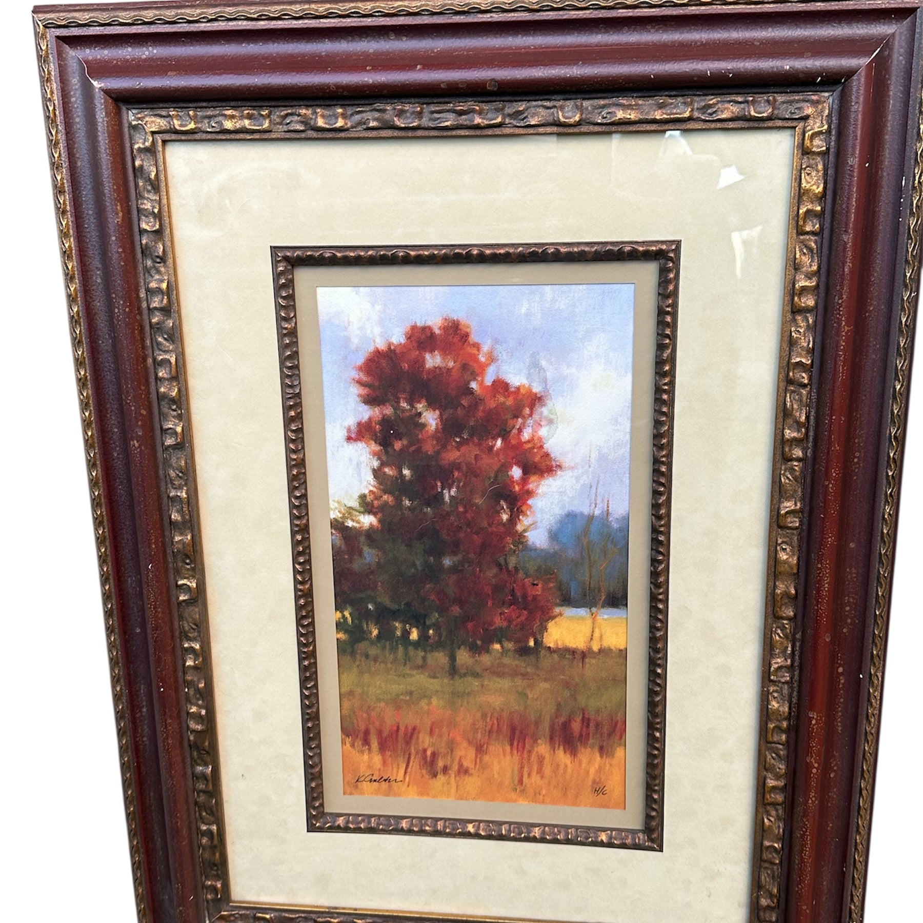 A framed painting features vibrant autumn trees in shades of red and orange, set against a soft blue sky and distant fields.