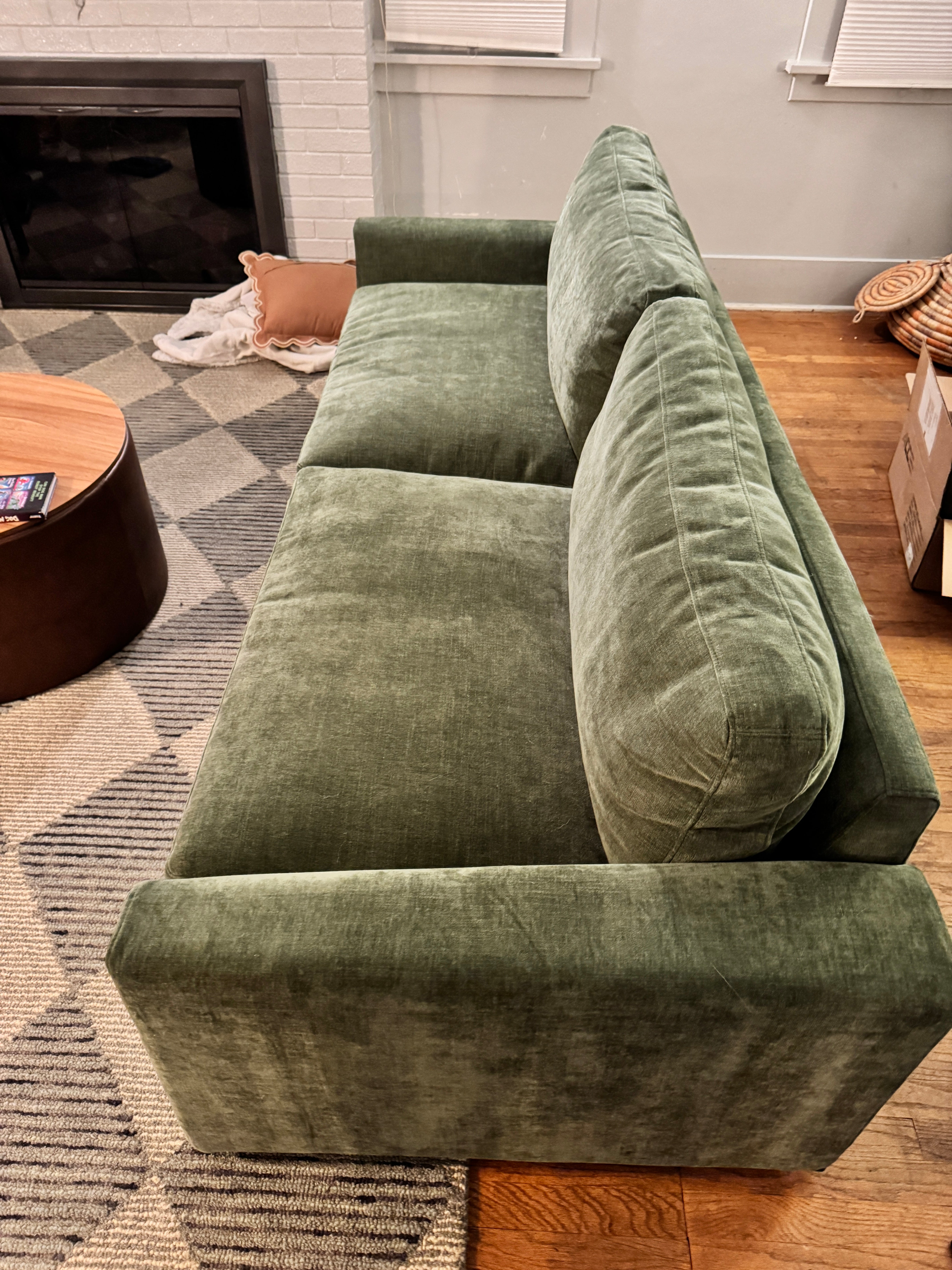 A green velvet sofa is positioned against a wall. A round wooden coffee table sits nearby, with a patterned rug beneath. Cozy pillows add warmth to the space.