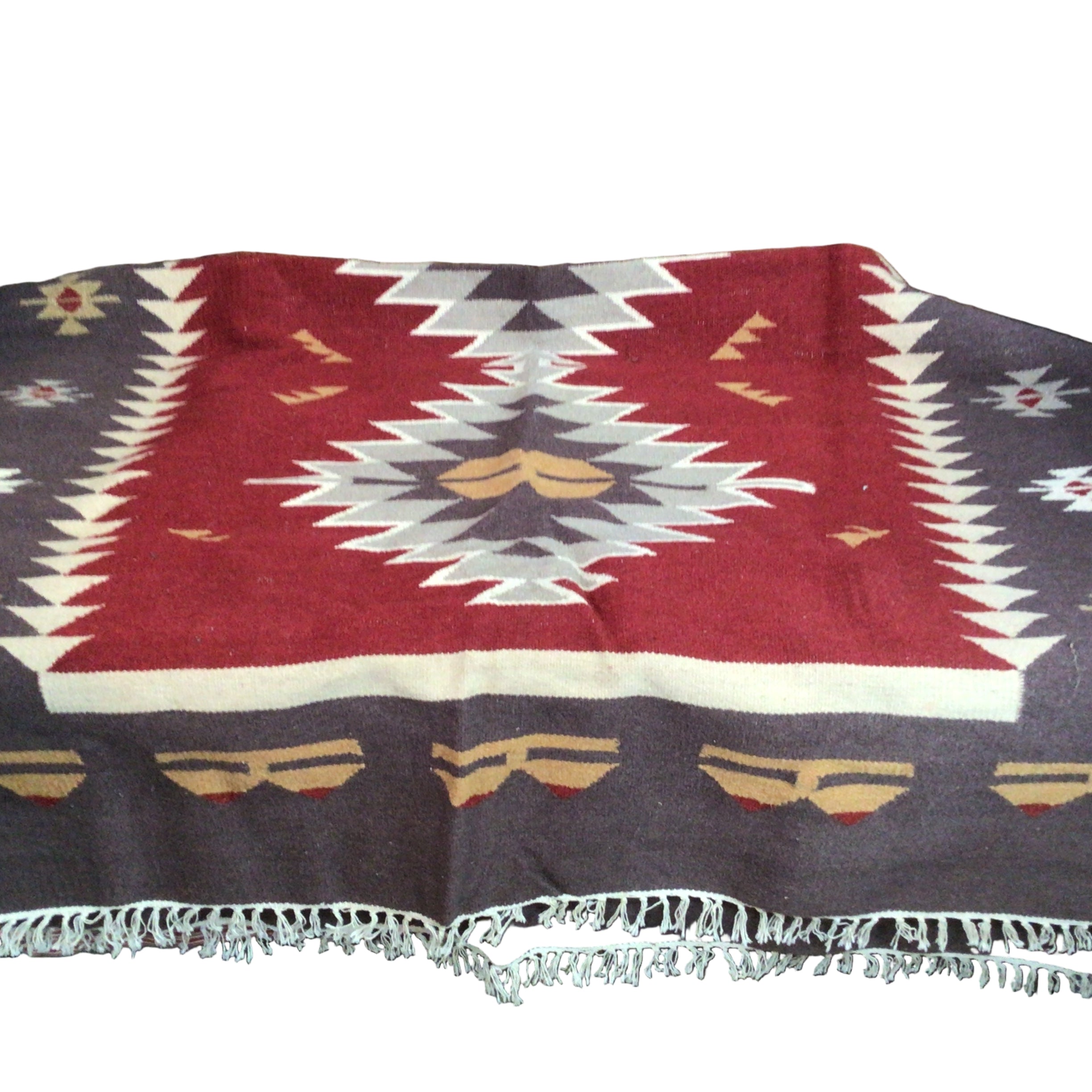 A patterned blanket featuring geometric designs in red, cream, and brown, laid on a surface, with fringed edges and a rustic wooden background.