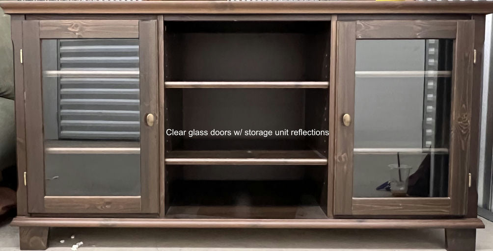 A wooden storage unit with clear glass doors, revealing three open shelving spaces. Reflections visible in the glass, showcasing a modern design.