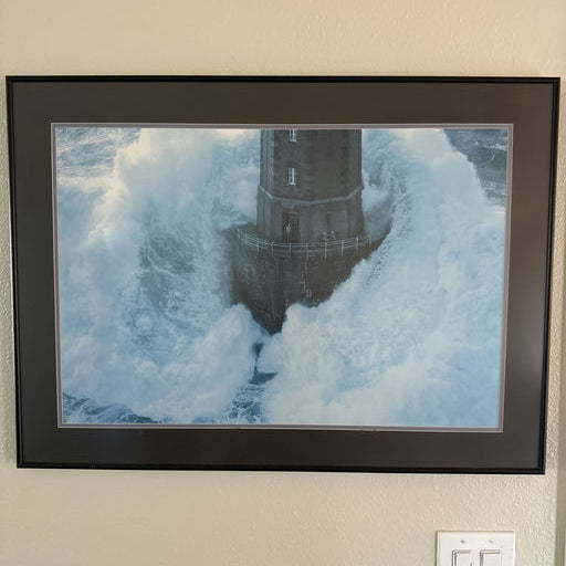 A lighthouse stands resilient amidst crashing waves, surrounded by turbulent seas, capturing the raw power of nature in a dramatic coastal scene.