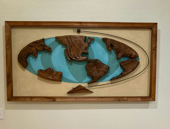 Wooden world map artwork featuring carved continents in earthy tones, set against a turquoise background and framed in wood.