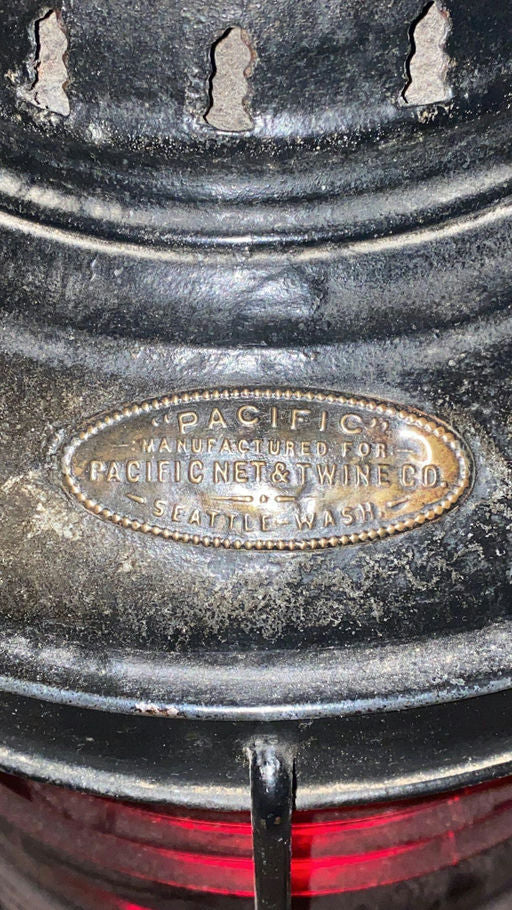 Close-up of a vintage lantern, showcasing the engraved plaque that reads "Pacific Manufactured for Pacific Net & Twine Co., Seattle, Wash."