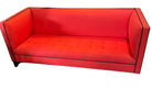 Bright red modern couch with black trim, featuring tufted upholstery. Set in a stylish interior with decorative plants and lamps in the background.