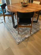 A round wooden dining table with four chairs sits on a patterned rug. A decorative bowl is placed in the center of the table.