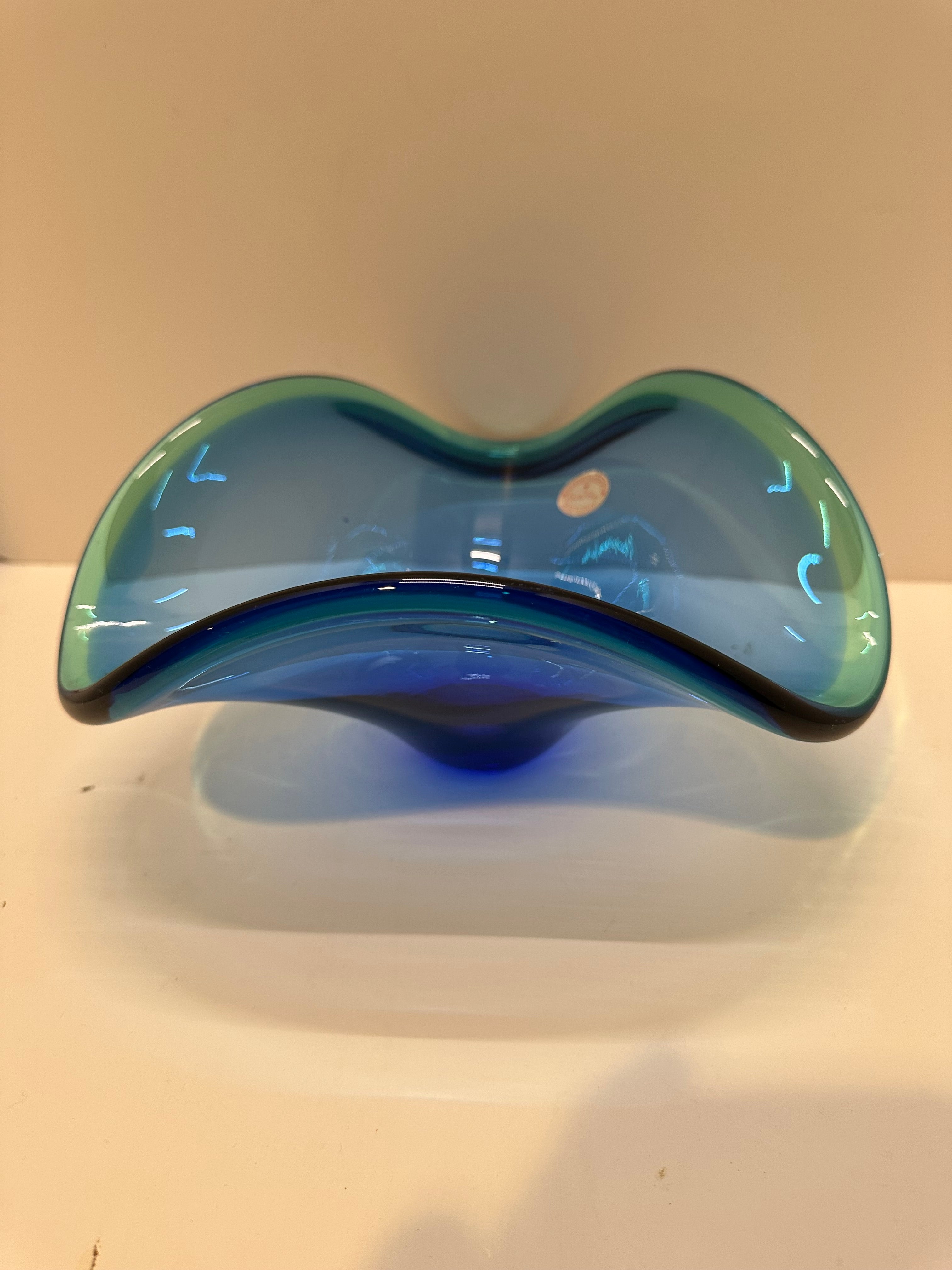 A wavy, two-toned glass vase in blue and green hues, featuring a smooth surface and a slight tapering at the base, placed on a white background.