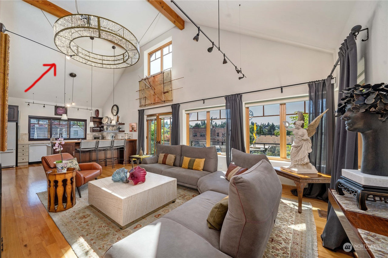 Bright living room featuring a large chandelier, modern furniture, and large windows. Decor includes a statue and colorful accent pillows.