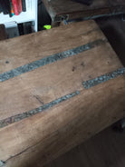 A close-up of a wooden table surface featuring natural grooves and metallic strips embedded in the wood, with a warm, rustic finish.