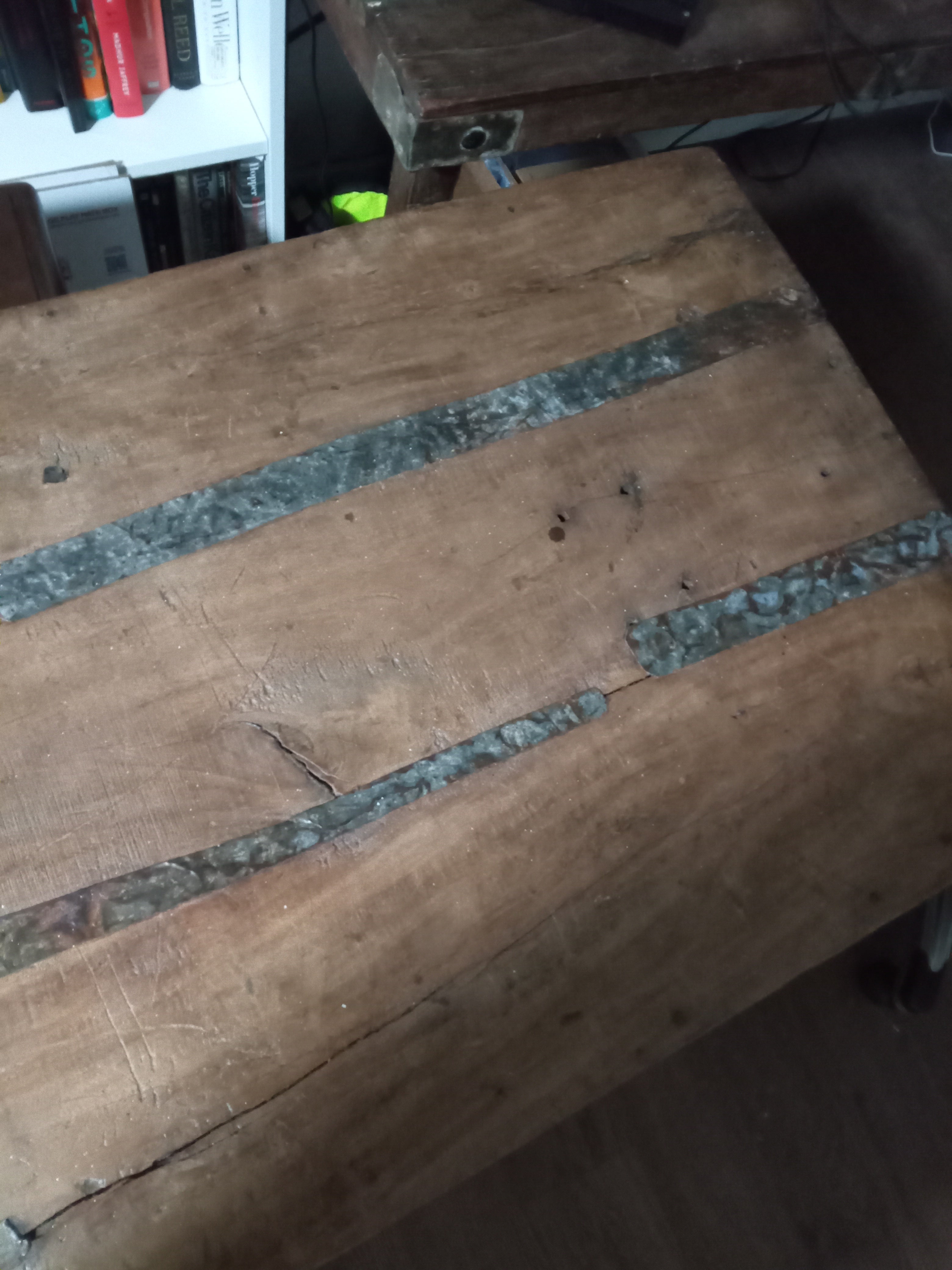 A close-up of a wooden table surface featuring natural grooves and metallic strips embedded in the wood, with a warm, rustic finish.