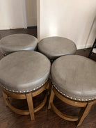 Four round stools with gray upholstery and decorative silver studs stacked closely together on a wooden floor in a well-lit room.