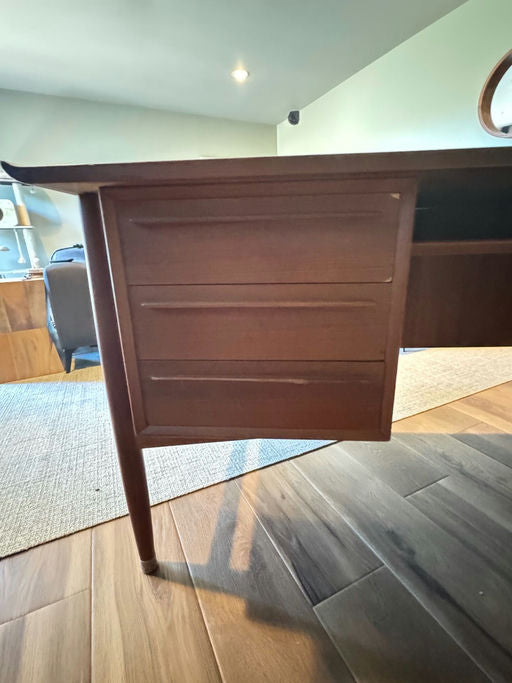 A wooden desk is shown from a low angle, highlighting its smooth finish and drawers. Soft lighting and a serene room atmosphere are visible.