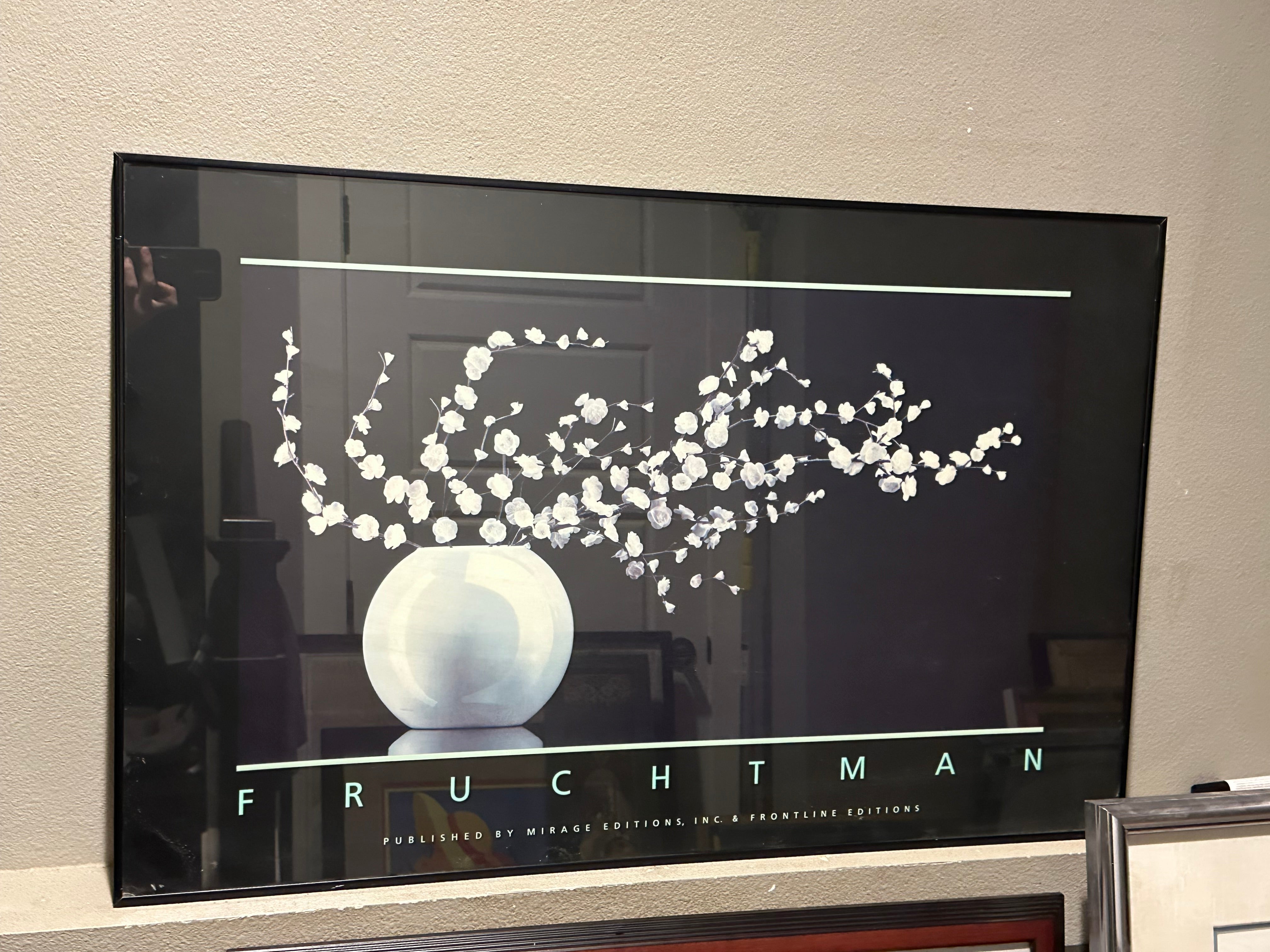 A framed poster features a minimalist design with white flowers in a round vase on a dark background, titled "FRUCHTMAN."