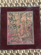 A framed artwork featuring intertwined Eiffel Towers with artistic text and sketches, set against a colorful background of pink and brown tones.