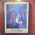 A colorful framed artwork by Marta Gilbert depicting women and children in a lush green setting, showcasing cultural and familial themes.
