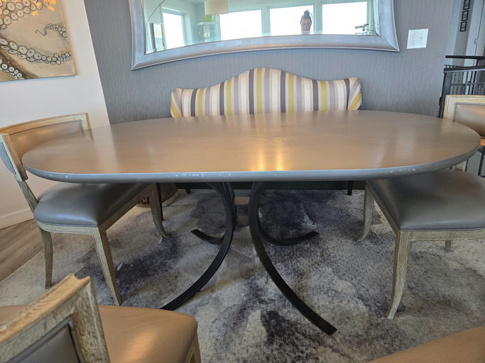 A modern dining area features an elliptical table with a sleek metal base, surrounded by light-colored chairs and a mirrored backdrop.