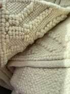Close-up of a textured cream-colored knitted blanket, showcasing its soft fibers and patterned surface, folded for a cozy appearance.