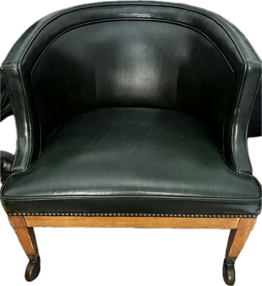 A vintage green leather armchair with a curved back and wooden legs, featuring decorative nailhead trim along the base for added elegance.