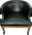 A vintage green leather armchair with a curved back and wooden legs, featuring decorative nailhead trim along the base for added elegance.