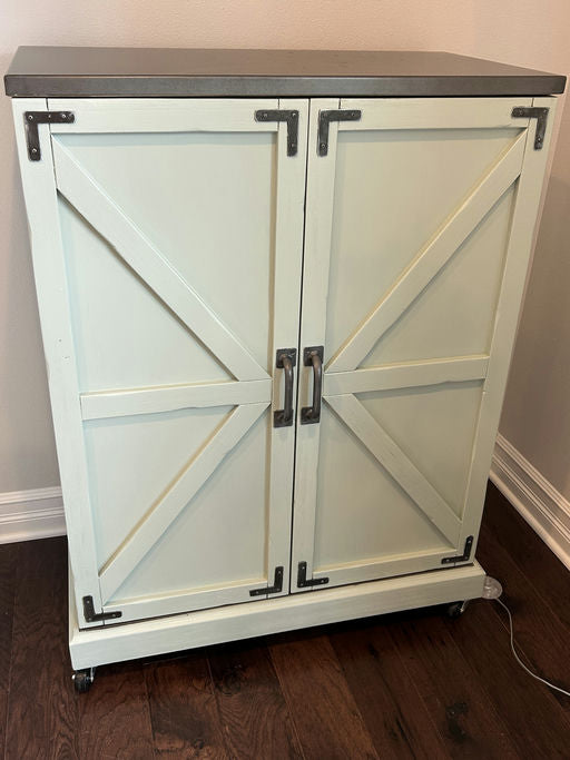 A mint green cabinet with a gray top features barn door style fronts and metal hardware. It sits on wheels for easy mobility on hardwood flooring.