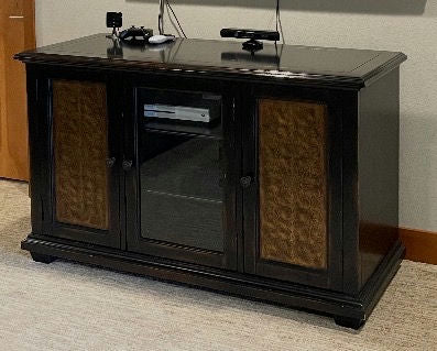A dark wooden entertainment cabinet with three compartments, featuring two decorative side panels and a glass middle door, on a carpeted floor.