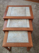 Three nested tables with wooden frames and textured stone-like surfaces, arranged on a carpeted floor, showcasing a simple, modern design.
