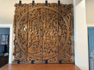 Intricate wooden wall art featuring figures, plants, and mythical creatures, elegantly carved with detailed scenes, set against a light background.